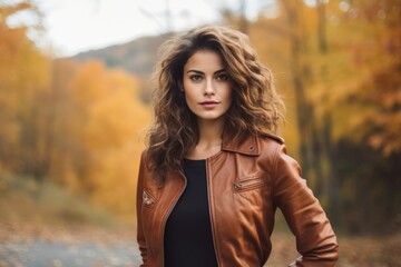A casually dressed woman in a brown leather bomber jacket enjoying the tranquility of a rural autumn afternoon, with a backdrop of colorful fall foliage