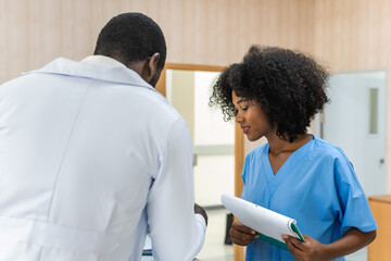 Black doctor man talking with black curly hair nurse at hospital registration counter 