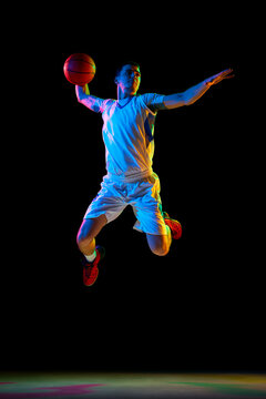 Athlete in jump pass in basketball, illuminated by colorful lighting. against black studio background in mixed neon light. Concept of professional sport, energy, strength and power, match, tournament.