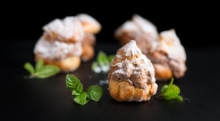 Profiteroles or cream puff with filling,  powdered sugar topping, on black background. Fresh homemade Cream Puffs, cake, tasty French choux puff, ecler, dessert closeup. Pastries