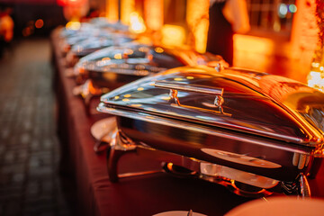 Riga, Latvia - February 16, 2024 - a row of shiny chafing dishes on a buffet table, reflecting the...