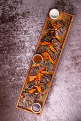 Wooden tray with delicious sliced beef and pumpkin on dark table