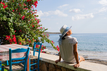 Woman with hat sitting enjoying a splendid summer day on her vacation next to greek tavern and the...