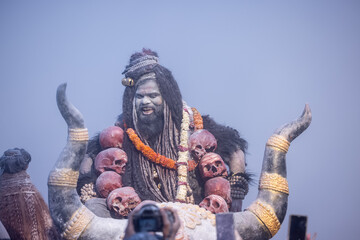 Masan Holi, Portrait of an male artist act as lord shiv with dry ash on face and body also in air while celebrating the holi festival as tradition at Harishchandra ghat in varanasi, India. - obrazy, fototapety, plakaty