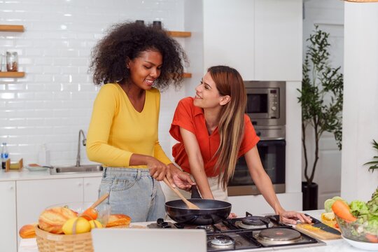 A couple of young girls friends laughing and having fun while cooking, Happy LGBT lesbian couple  cooking together at home