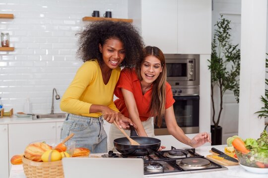 A couple of young girls friends laughing and having fun while cooking, Happy LGBT lesbian couple  cooking together at home
