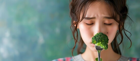 unhappy asian women is on dieting time looking at broccoli on the fork girl do not want to eat vegetables and dislike taste. with copy space image. Place for adding text or design - obrazy, fototapety, plakaty