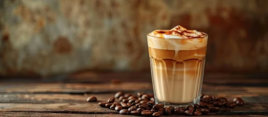 Poster Caramel macchiato coffee milk and caramel drink in glass on wooden table with coffee beans sweet drink cafe food menu copy space for text. with copy space image. Place for adding text or design © vxnaghiyev