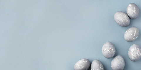 Festive Easter background. Gray-blue Easter eggs with stars on a blue table. Banner with a place...