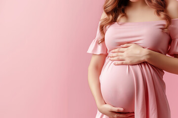 Pregnant woman in a pink dress holding her belly on a pink background.