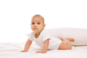 Beautiful baby, little girl in white comfortable clothes lying on belly on bed with pillow behind against white background. Concept of childhood, family, care, motherhood, infancy, heath