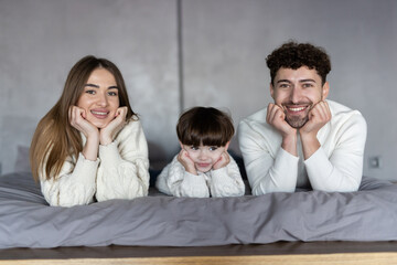 Happy family looking at the camera on their bed at home