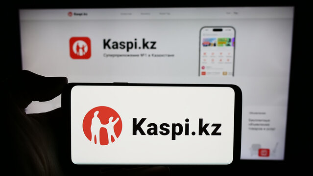 Stuttgart, Germany - 02-13-2024: Person holding mobile phone with logo of Kazakh financial services company Kaspi.kz in front of business web page. Focus on phone display.