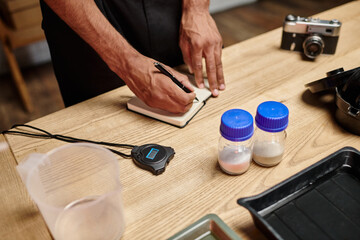 cropped view of african american man taking notes near bottles with film developing powder