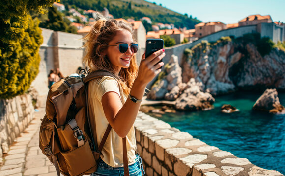 Adriatic Elegance: A Young Native Woman, Backpack-Clad and Radiantly Smiling, Takes a Selfie in Dubrovnik, Croatia, a UNESCO Heritage City, Immersed in Historic Splendor by the Adriatic Sea.


