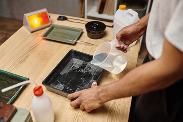 cropped photo of african american man pouring chemical solution for film development in tray