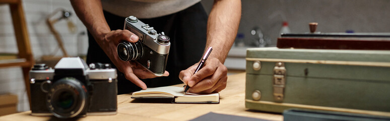 cropped banner of african american photographer immersed in writing holding his analog camera