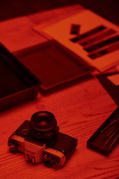 A darkroom table with analog camera and tools for film development under the glow of red light