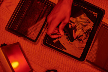 top view of photographer taking freshly developed photo paper in chemical solution with tweezers