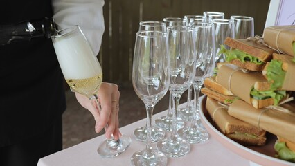 Catering with sandwiches. A young woman pours champagne into glasses.