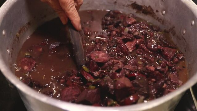 hands stirring a pan with feijoada, typical Brazilian food