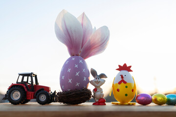 small toy red tractor, a large Easter egg with a magnolia flower, a souvenir bunny, candy at...