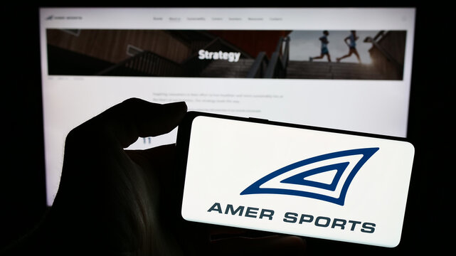 Stuttgart, Germany - 02-15-2024: Person holding cellphone with logo of Finnish sporting equipment company Amer Sports Oyj in front of business webpage. Focus on phone display.