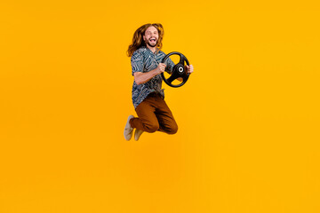 Full length photo of impressed excited guy wear print shirt jumping high riding car isolated yellow color background