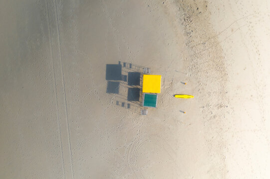 Aerial view of a yellow lifeguard chair and rescue board on a beach at sunrise with long shadows casting from the chairs, Durban, Kwa Zulu Natal, South Africa.