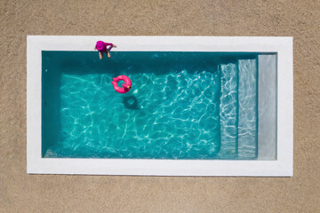 Aerial view of a girl wearing a pink costume sitting by a pool with clear blue water and a pink flamingo floatie in the pool, Cape Town, Western Cape, South Africa.