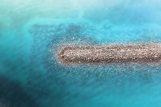 Aerial view of a barrier wall in the crystal clear blue ocean with patterns of rocks visible underneath the water, creating an abstract image, Dubai, Dubai, United Arab Emirates.