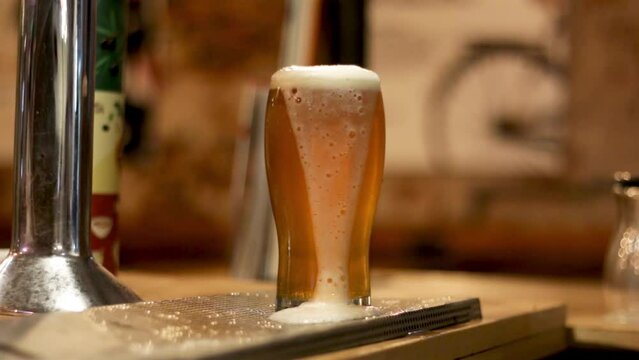 Cerveza tirada artesanal servida en un bar. Vaso lleno de cerveza tirada artesanal con espuma derramada. Pinta de cerveza tirada