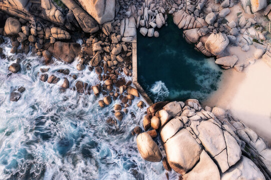 Aerial view of a tidal rock pool, taken with a long exposure shutter setting, showing the waves crashing onto the rocks and flowing into the pool, Cape Town, Western Cape, South Africa.