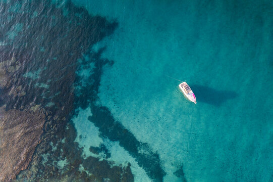 Aerial view of a small fishing boat in blue tropical water with a reef visible in the water, Port Willunga, South Australia, Australia.
