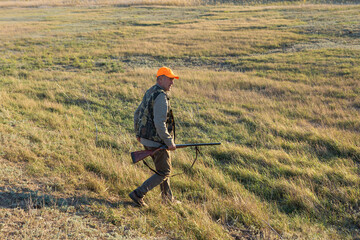 Mature man hunter with gun while walking on field.
