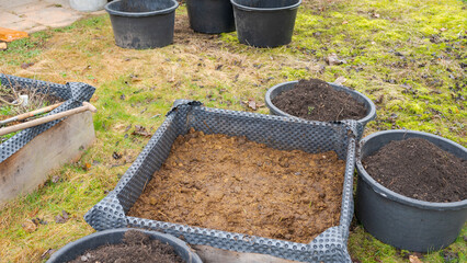 Raised bed in garden filled with horse manure as fertilizer with buckets of soil around it