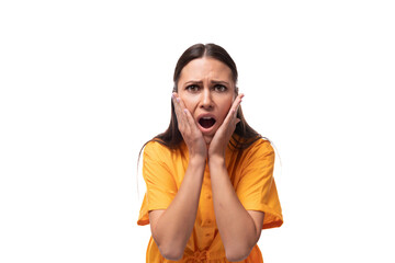European young woman with black hair dressed in an orange summer dress looks at the camera with surprise and fear