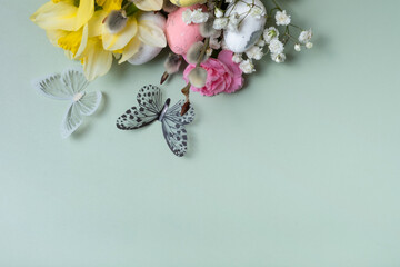 Butterflies and yellow daffodils, easter eggs and willows twigs on green background with copy space