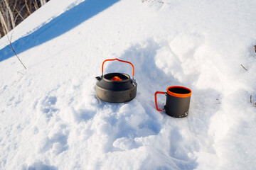 Tourist utensils stand on the snow in the winter forest, a kettle with a mug made of metal, a halt...