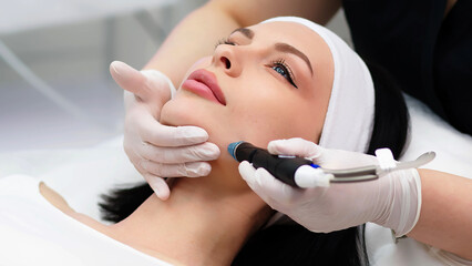 A professional dermatologist wearing medical gloves performs a hydropeeling procedure on a young woman in a professional beauty salon.