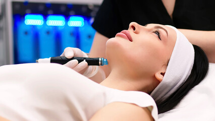 A professional dermatologist wearing medical gloves performs a hydropeeling procedure on a young...