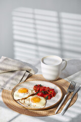 Breakfast with fried eggs and fried tomatoes with spinach on plate and cup of latte coffee