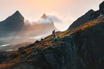 Man climbing mountains traveling in Norway tourist solo hiking in Lofoten islands outdoor traveler with backpack active healthy lifestyle adventure summer vacations - obrazy, fototapety, plakaty