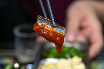 Close-up of half-dried saury with hot sauce held up with chopsticks