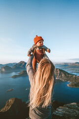 Mother holding up infant baby outdoor family lifestyle traveling in Norway summer vacations blonde woman with child exploring Lofoten islands - 741701229