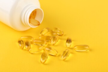 Vitamin capsules and medical bottle on yellow background, closeup