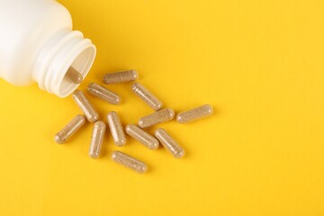 White medical bottle and vitamin capsules on yellow background, top view. Space for text