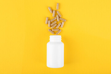 White medical bottle and vitamin capsules on yellow background, top view
