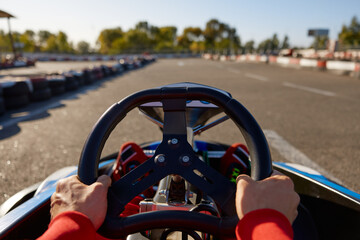 Closeup go-kart racer driving sportcar, focus on hands holding steering wheel