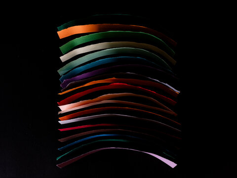 Abstract stack of strips of multi coloured paper against a black background